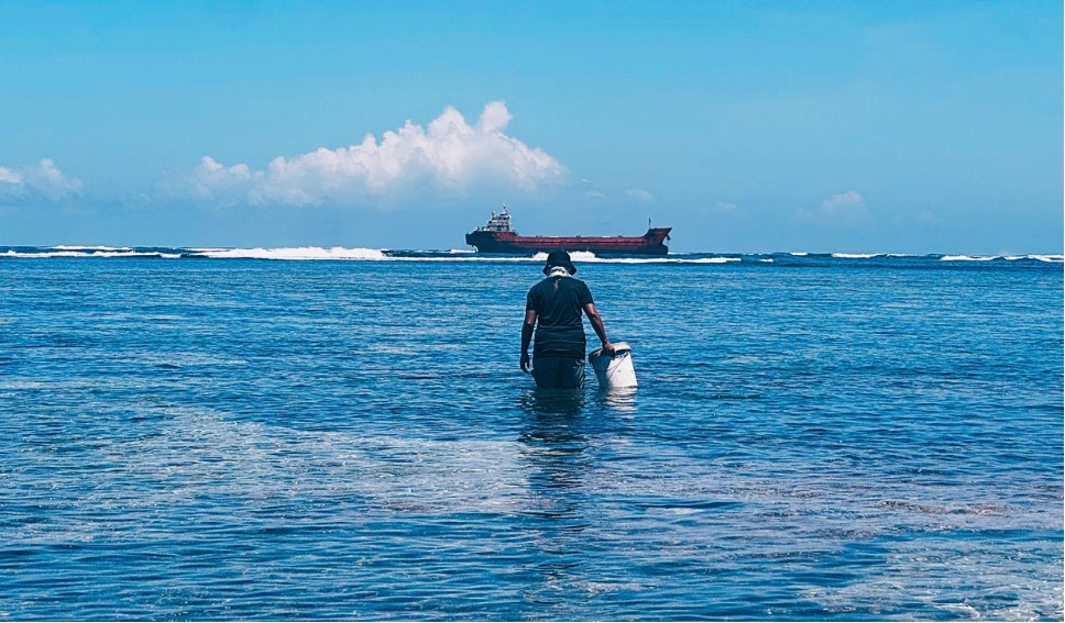 Fisherman wading in the shallows, the tanker behind